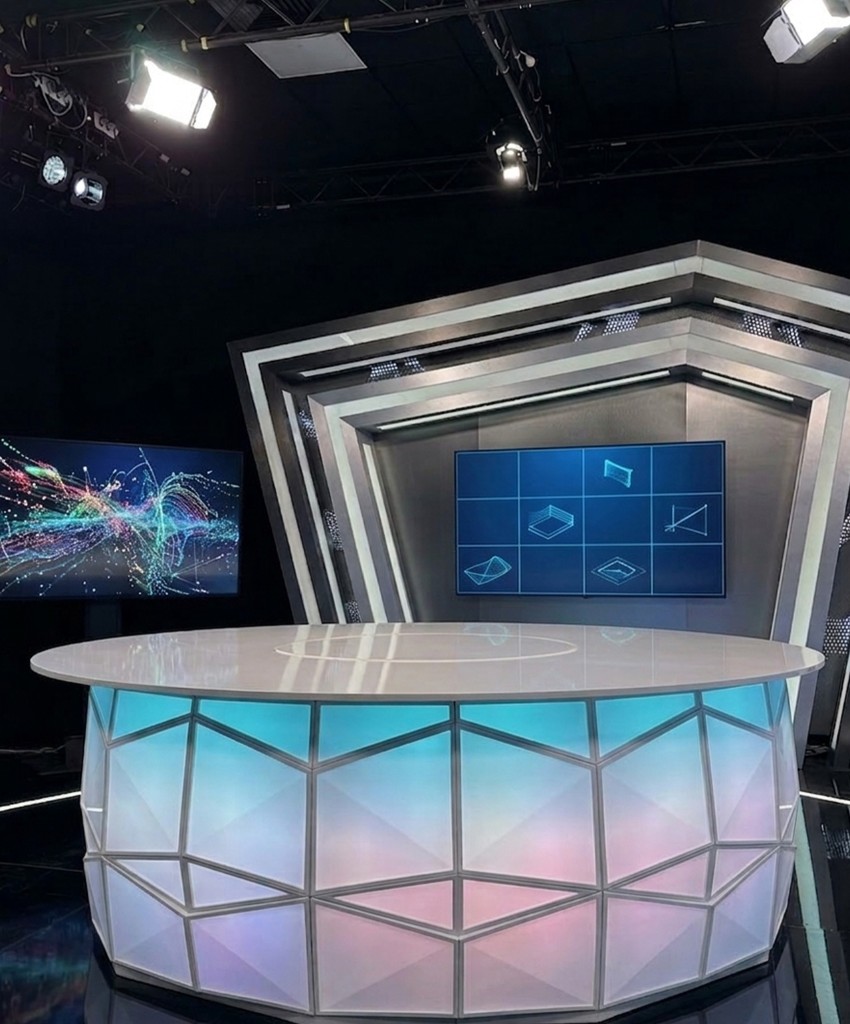 Custom TV news studio designed and built in Morocco — illuminated polygonal anchor desk, video wall, motion-graphics monitor and broadcast lighting plot